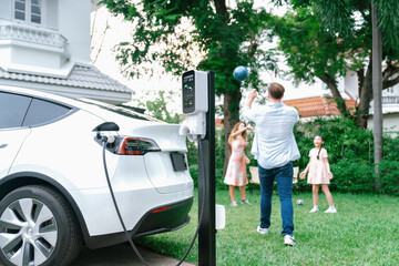 Focus electric vehicle recharge from home charging station on blur background of happy and playful...