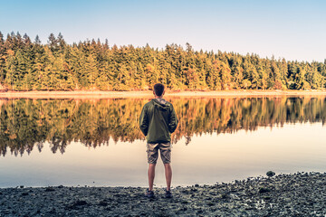 Male traveler  feeling at peace standing looking out at a beautiful mountain forest lake nature setting 