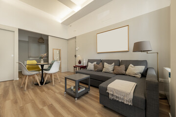 Living room of a small loft-type home with sofa with chaise longe upholstered in dark gray fabric, circular dining room measurements and light parquet floors