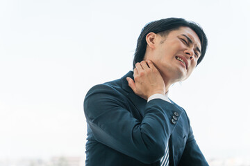 辛い首こり・肩こりに悩む若いアジア人ビジネスマン（疲労・緊張・運動不足）
