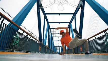 Professional break dancer perform street dance footstep at bridge. Asian hipster wear headphone while doing freeze pose. Break dancer, street dancer freestyle concept. Outdoor sport 2024. Sprightly.