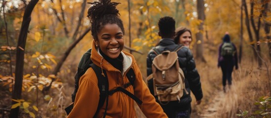 Smiling multiethnic teens holding hands while hiking in fall woods. - obrazy, fototapety, plakaty