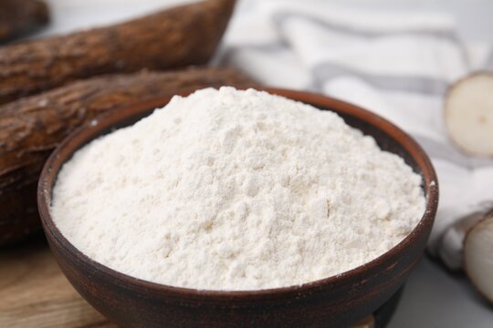 Bowl with cassava flour and roots on table, closeup