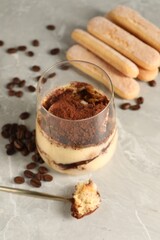 Tasty tiramisu in glass, coffee beans, spoon and biscuits on light grey table, closeup