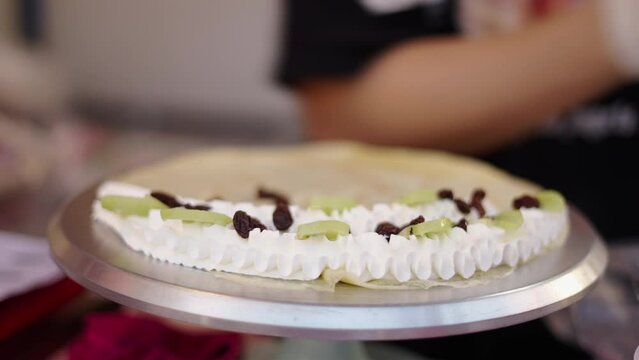 Hands preparing a crepe with cream and fruit