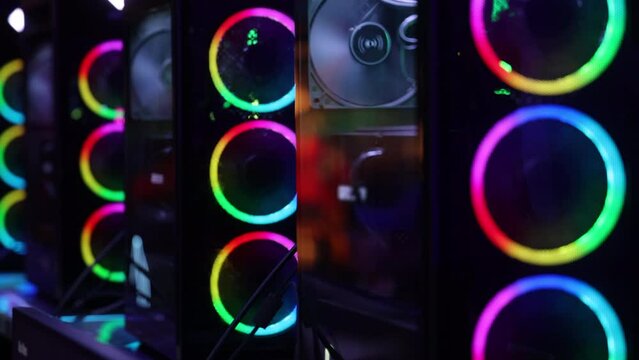 Row of high-performance gaming PC towers with bright RGB fans changing their different colors, showcasing powerful hardware. Slow Motion, Camera 4K RAW. 