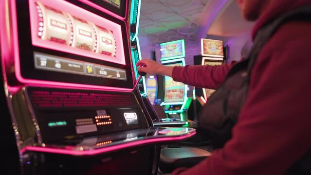 Caucasian Man in his 30s Playing Classic vintage casino slot machine winning jackpot loop Inside One of the Las Vegas Casino. Colorful Gambling Industry Theme. One Armed Bandits in slow motion