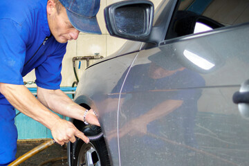 a young white latin man washing the inside of the fender of a car