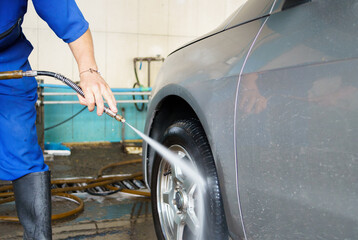 a man washing the front wheel of a gray car