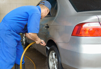 a man washing the wheels of a gray vehicle