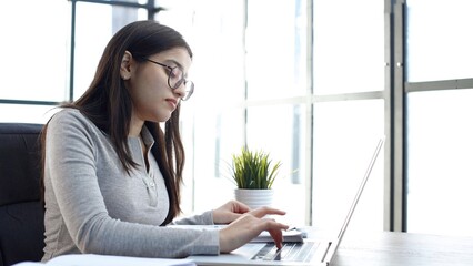 A young woman with glasses in the office is working with a laptop
