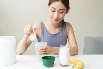 Young sporty woman pouring protein powder into a cup to make replacement food meal after workout