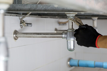Technician plumber using a wrench to repair a water pipe under the sink. Concept of maintenance,...