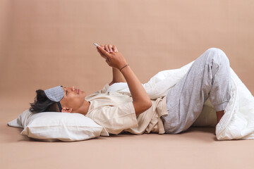 Young Asian man in pajamas, wear sleep mask, lay down and using mobile phone before sleeping