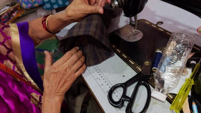 Closeup of a women tailor hands working on a sewing machine with fabric and scissors on a table