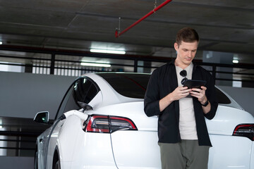 Young man travel with EV electric car to shopping center parking lot charging in downtown city...