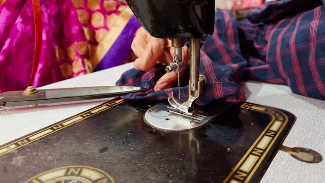 Closeup of a women tailor hands working on a sewing machine with fabric and scissors on a table