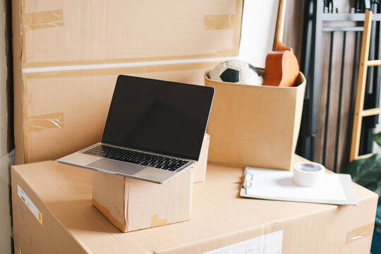 Background image of opened laptop with blank screen on cardboard boxes in new home, moving and relocation concept.