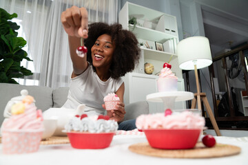 Beautiful young African blogger presenting piece of cupcake in concept showing special cuisine in pastel color. Content creating of social media with favorite sweets bakery dish. Tastemaker. - obrazy, fototapety, plakaty