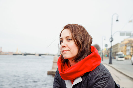 young caucasian female woman looks dreamily at city river of european city. lifestyle portrait of 38 years old woman. loneliness, sadness, dreams concept.