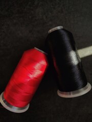 Red and white spools of thread are placed on a dark gray slate. Sunlight shines from the side.