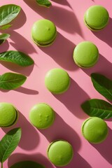 Top view of vibrant green macarons scattered among fresh leaves on a pink surface
