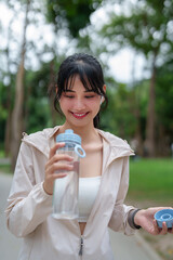 Young asian sporty women wearing bluetooth headphone to listening the music and drinking fresh water after jogging training and workout exercise for healthy wellness in the morning at outdoor park