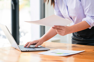 Businesswomen reading document and typing data on laptop while thinking about strategy of startup