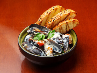 Mussels in creamy sauce with bread on a plate.