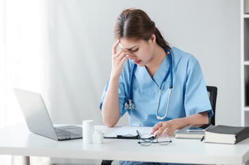 Asian female doctor working on laptop, filling out paperwork, patient medical history, reviewing documents at her workplace medical and health concept