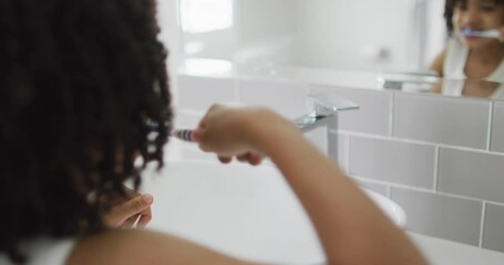 Biracial boy brushes teeth in a bright bathroom