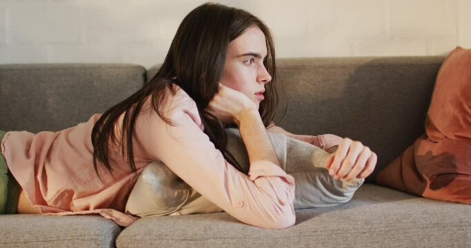 Young Caucasian transgender woman lounges on a sofa at home, looking thoughtful