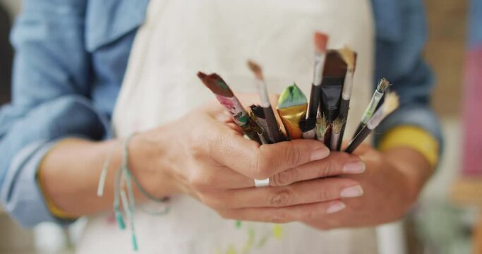 Artist's hands holding a variety of paintbrushes, with copy space