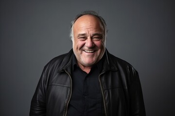 Portrait of a smiling senior man wearing a leather jacket on a grey background