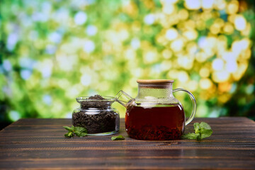 natural organic herbal tea in glass teapot and jar with dry tea on a wooden table