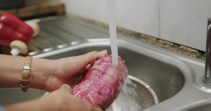 Hands rinse fresh meat under tap water in a kitchen sink