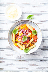 Penne pasta with yellow and red pepper, hard cheese and fresh basil. Bright background. Top view.	
