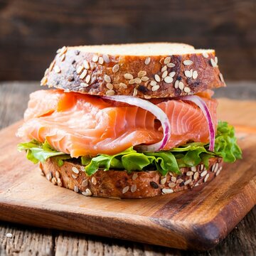 Healthy sandwich with rye bread bun, salmon, avocado, onion and salad served on a wooden rustic board.