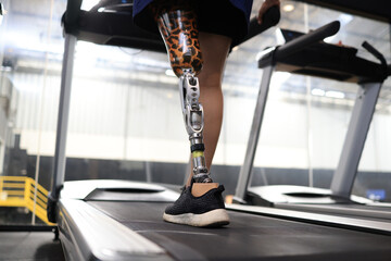 Low angle view at woman with prosthetic leg walking in treadmill at fitness gym