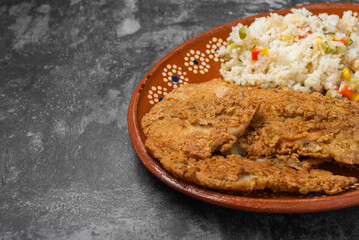 Breaded fried fish and rice in a clay dish on a wooden table.