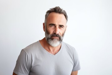 Portrait of handsome mature man with grey beard looking at camera while standing against grey background
