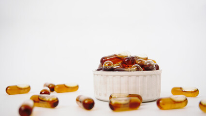 Brown liquid gel medicine fish oil omega capsule stacked on a bottle cap on a white background