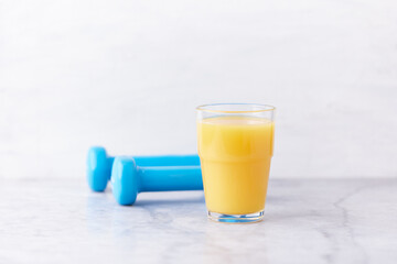 Glass of Orange Juice and Blue Dumbbells in background. Stone background. Close up.	