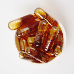 Brown liquid gel medicine fish oil omega capsule stacked on a bottle cap on a white background