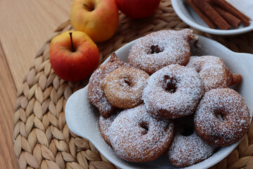 Deep fried apple rings with batter sprinkled with powdered sugar ona white plate on wooden table with fresh apples