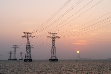 High voltage electricity tower in the ocean at sunset