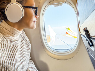 Side view of female passenger inside airplane flight looking outside the window the wing and blue...