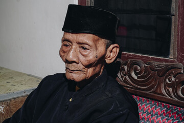 Fototapeta premium Thoughtful senior Asian man sitting on home sofa, looking away with thoughts, thinking over future retirement, planning, dreaming