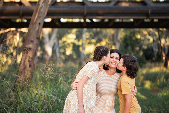 Portrait of kids kissing mother on cheek in Australian bush setting