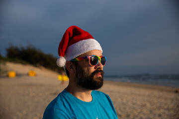 man wearing a santa hat and rainbow glasses at the beach